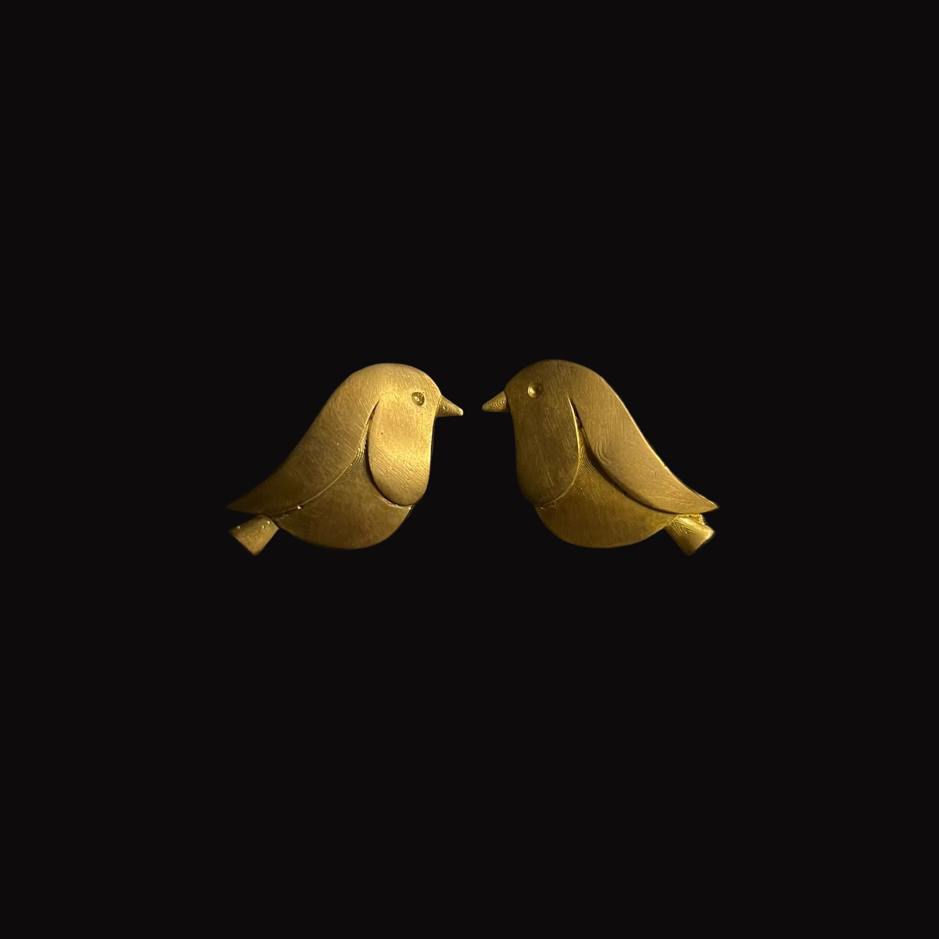 Pair of gold bird-shaped earrings on a black background